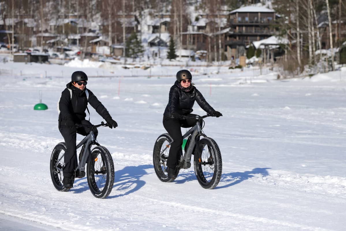 Kaksi talvipyöräilijää järven jäällä. Taustalla hotelli Järvisydän.