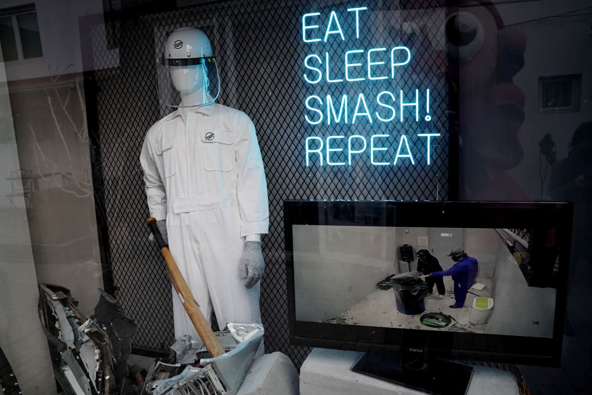 Eat sleep smash repeat -loisteputkikyltti seinällä, vieressä valkoiseen haalariin puettu mallinukke.