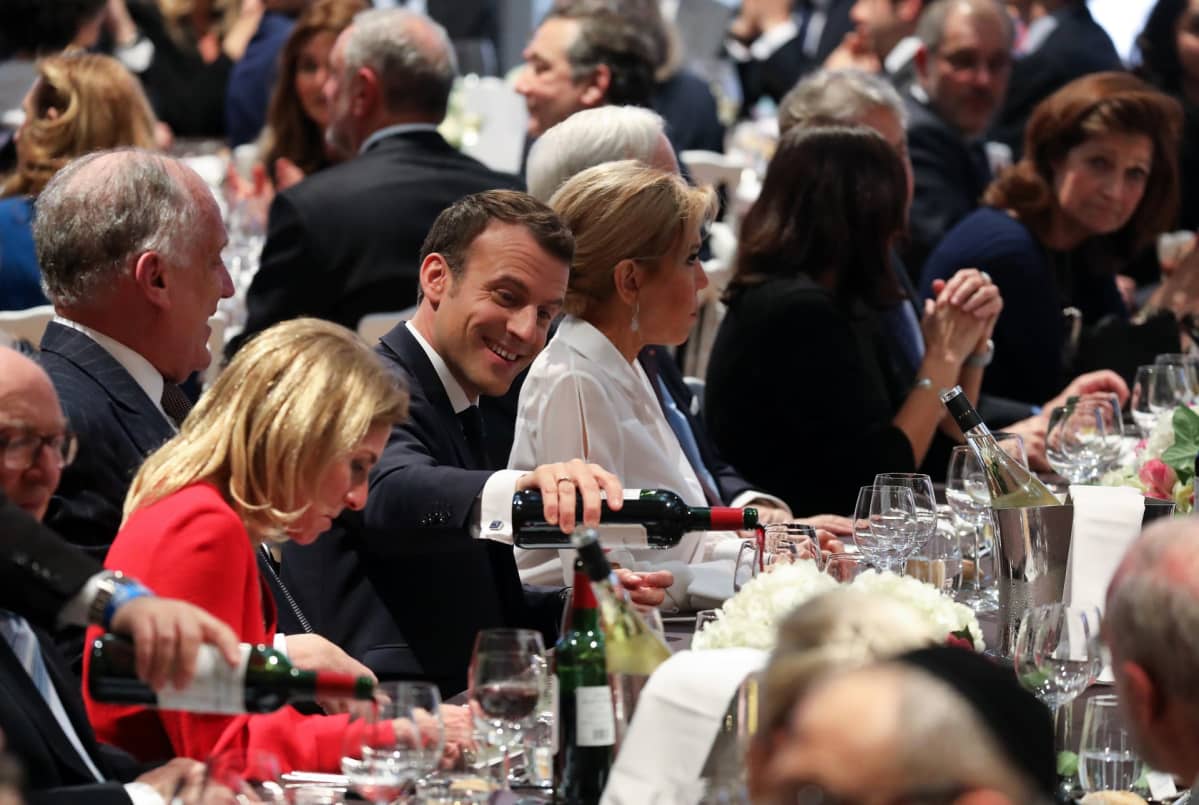 Ranskan presidentti Emmanuel Macron istuu illallispöydässä ja kaataa itselleen viiniä.