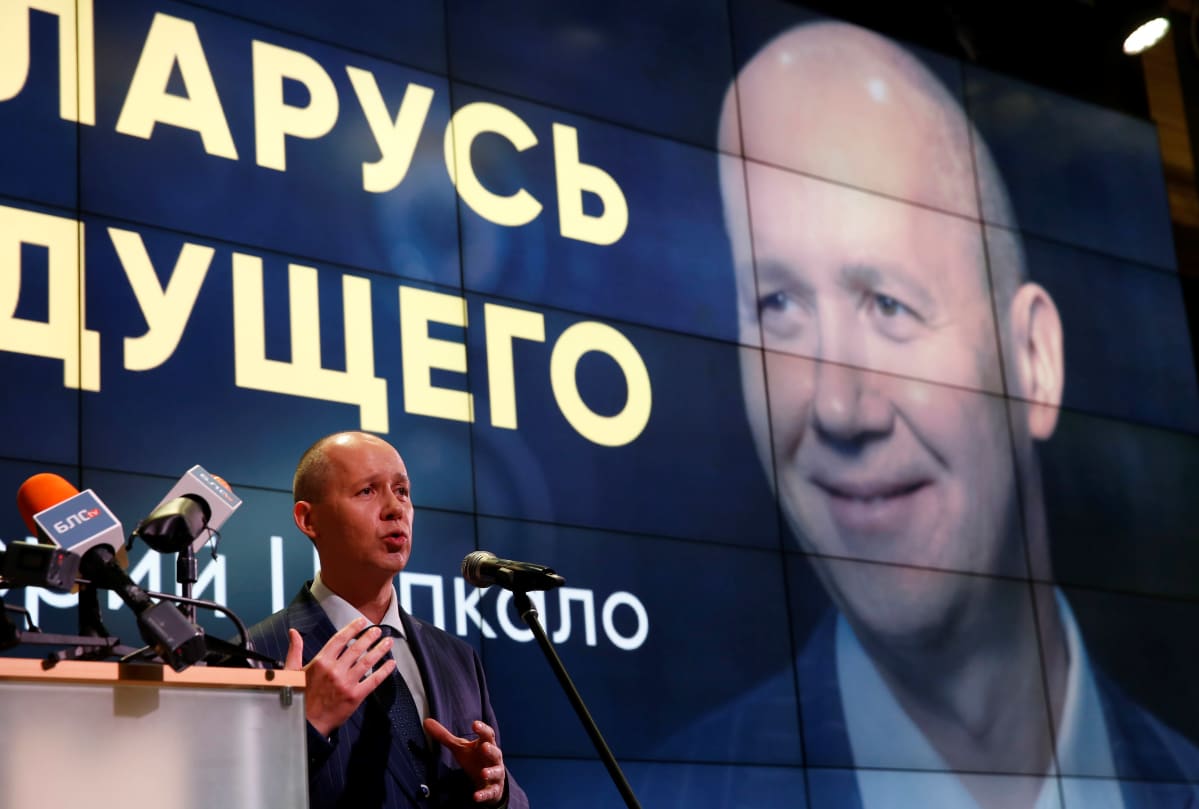 Valery Tsapkala puhuu suuren näytön edessä. Näytöllä on suuri kuva hänestä.