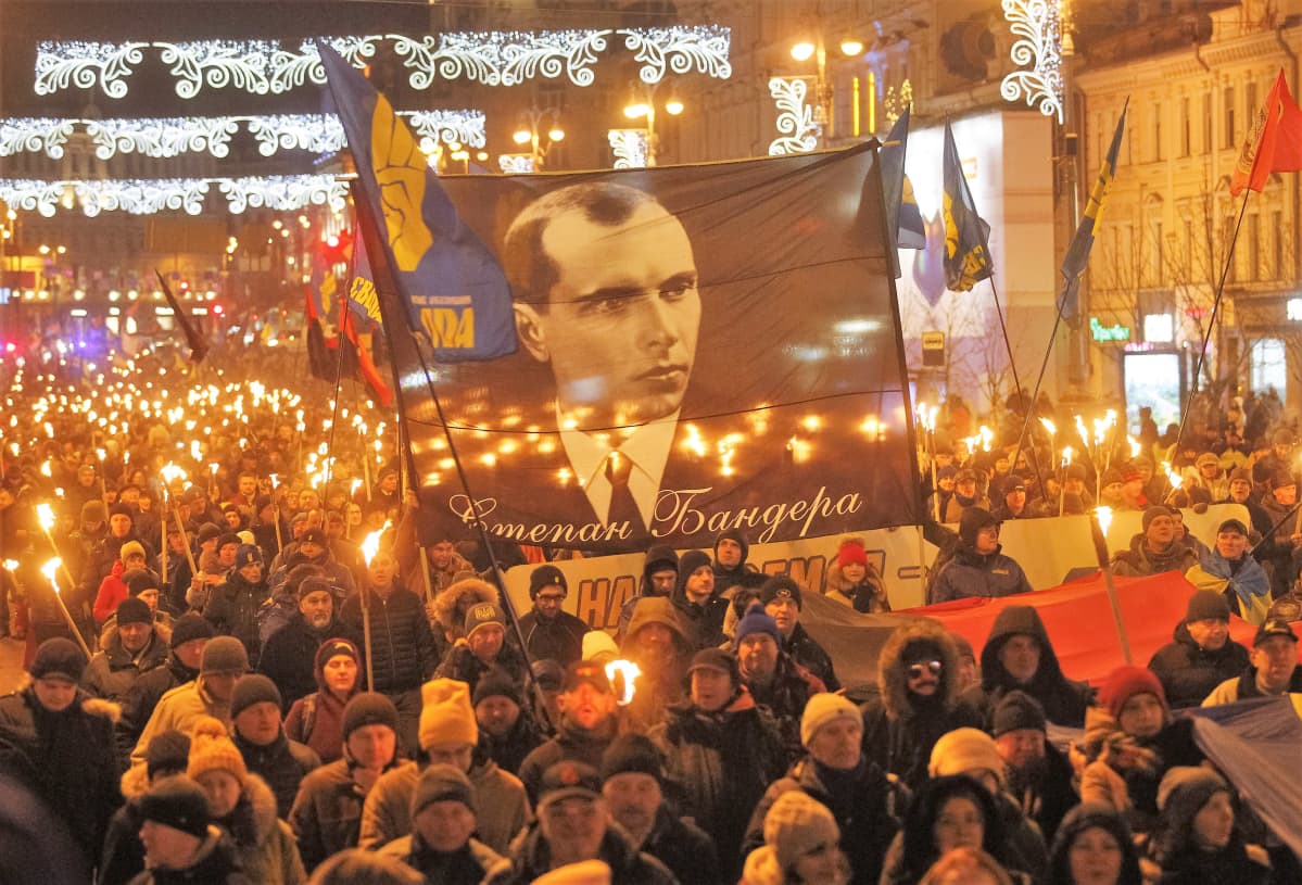 Soihtukulkue marssii kadulla. Marssijoilla on suuri plakaatti, jossa on Stepan Banderan kuva.