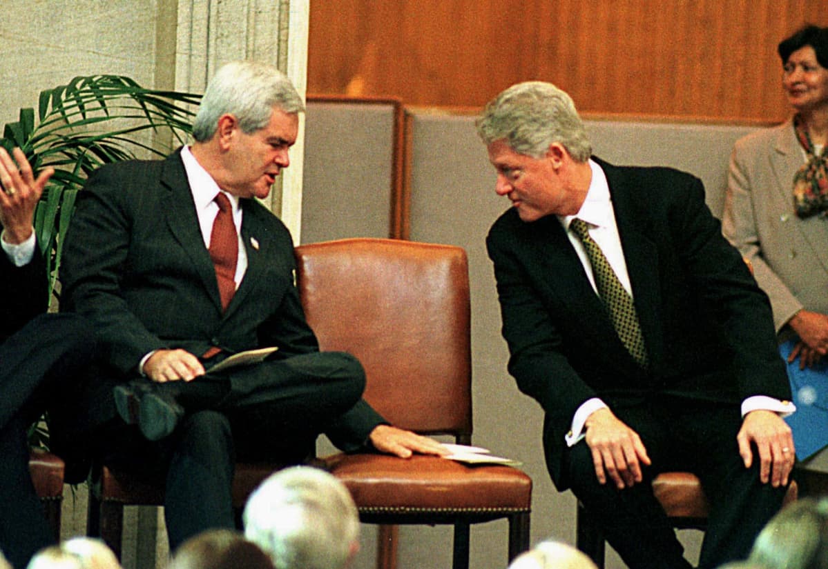 Newt Gingrich ja presidentti Bill Clinton istuvan vaivaantuneen näköisinä, välissä tyhjä tuoli.