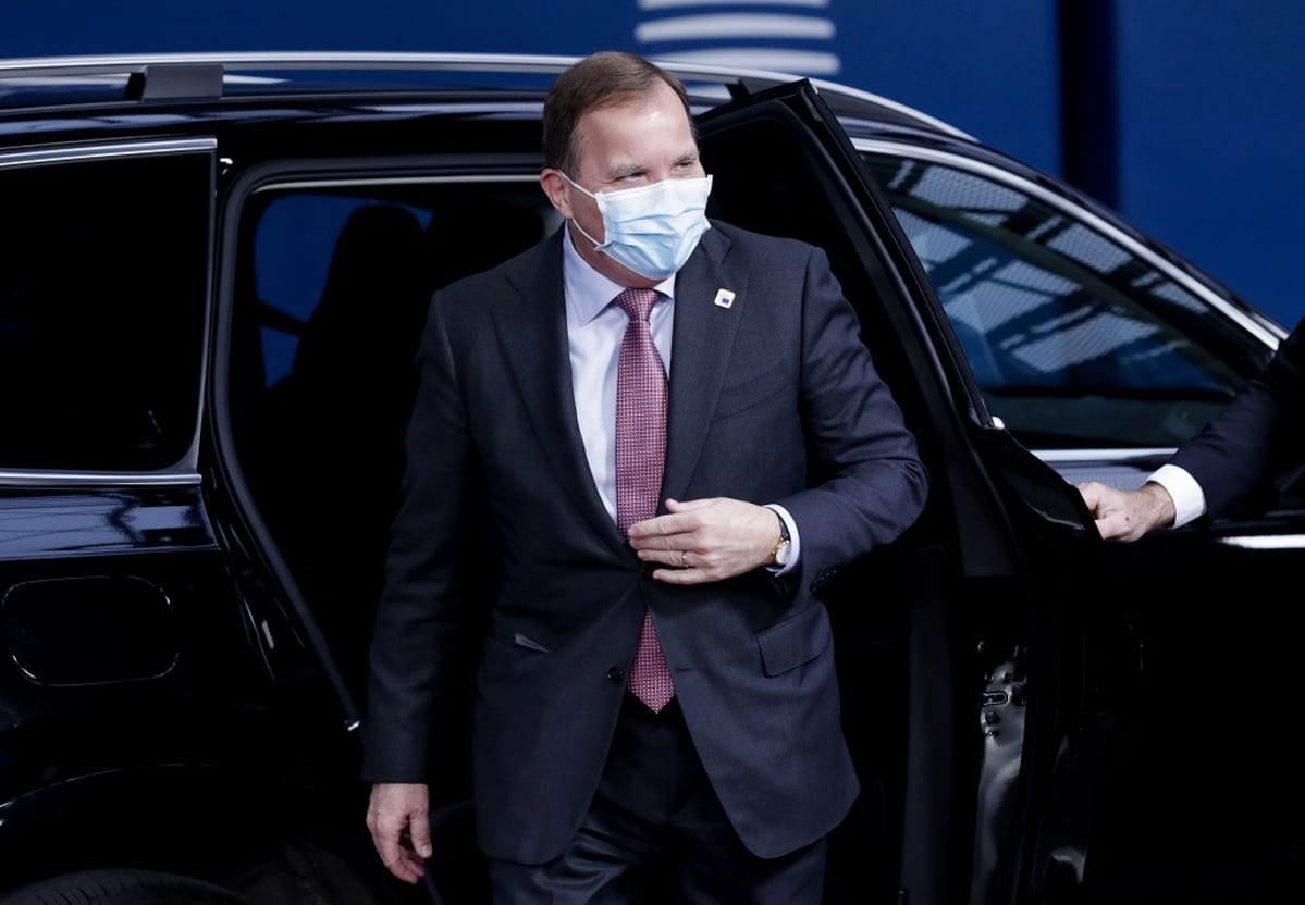 Löfven avoin autonovi takanaan, päällä puku, kasvoilla maski.