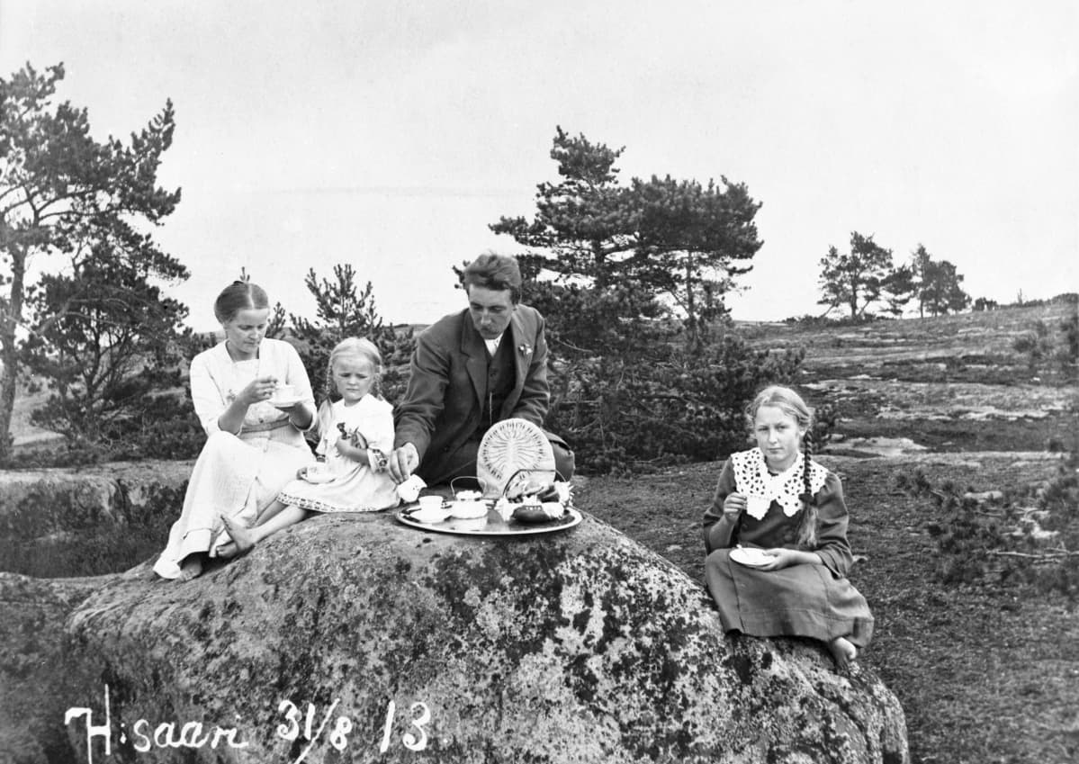 Perhe istuu kalliolla kahvikupit kädessä
