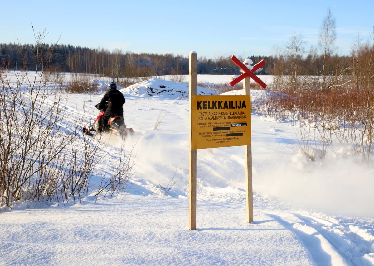 moottorikelkkailija ajaa kelkkareitistä kertovan merkinnän ohi