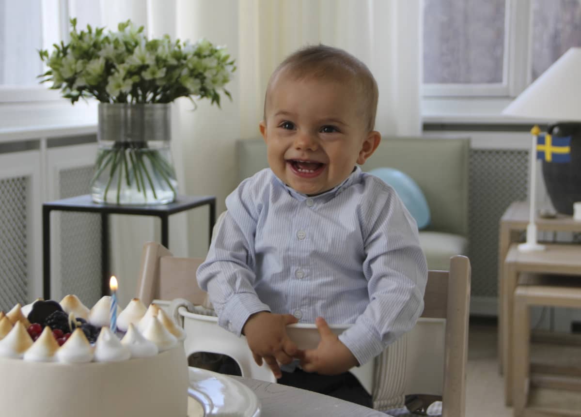 Oscar hymyilee syöttötuolissa, edessä kakku, jossa yksi kynttilä.