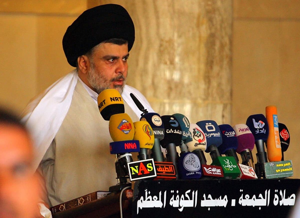 Muqtada al-Sadr seisoo puhujankorokkeen takana musta turbaani päässään ja puhuu mikrofoneihin.