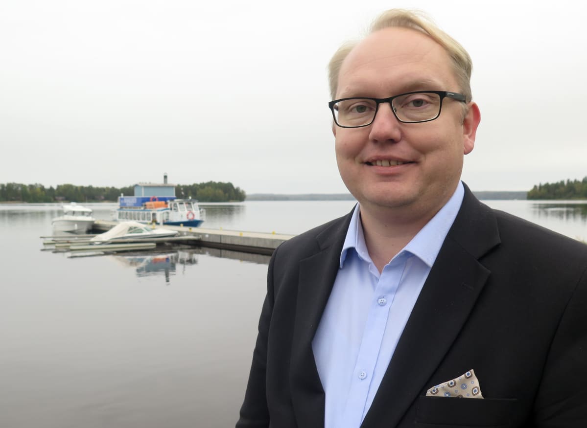 Kaupunginjohtaja Kari Tolonen seisoo järven rannalla ja hymyilee.