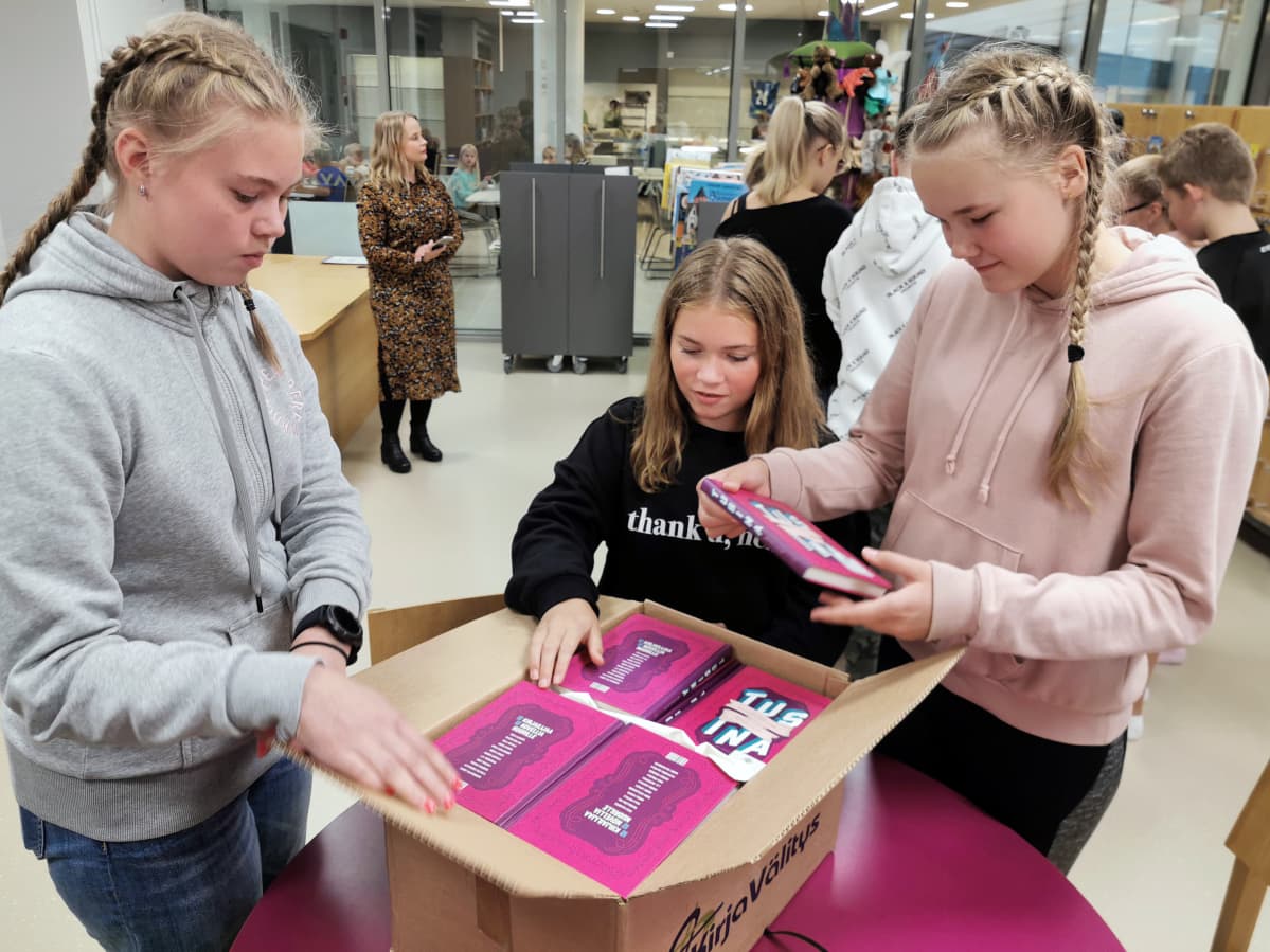 Koululaiset avaavat pahvilaatikkoa, jossa on lahjoituskirjoja.