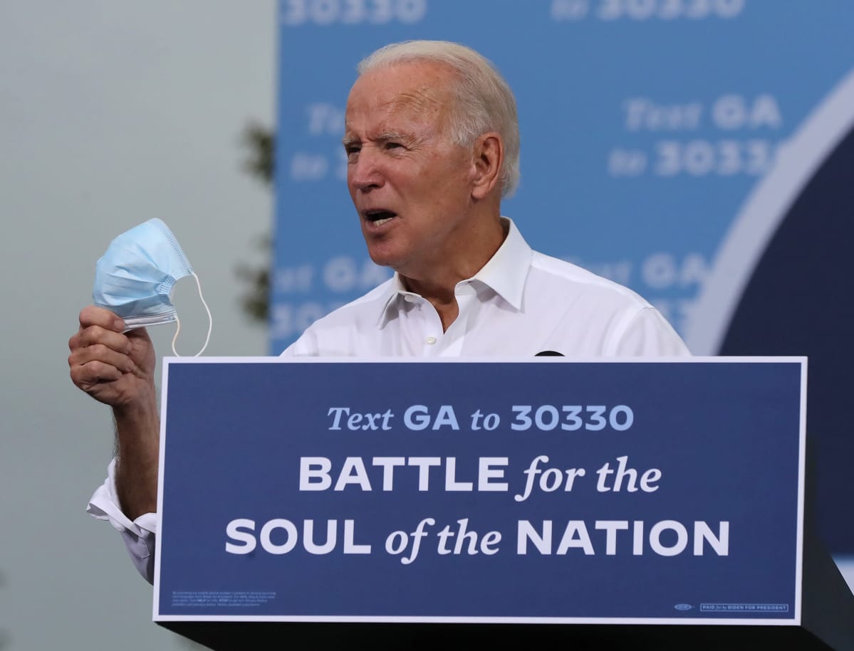 Joe Biden puhuu kannattajilleen. Hänellä on oikeassa kädessä kasvomaski.