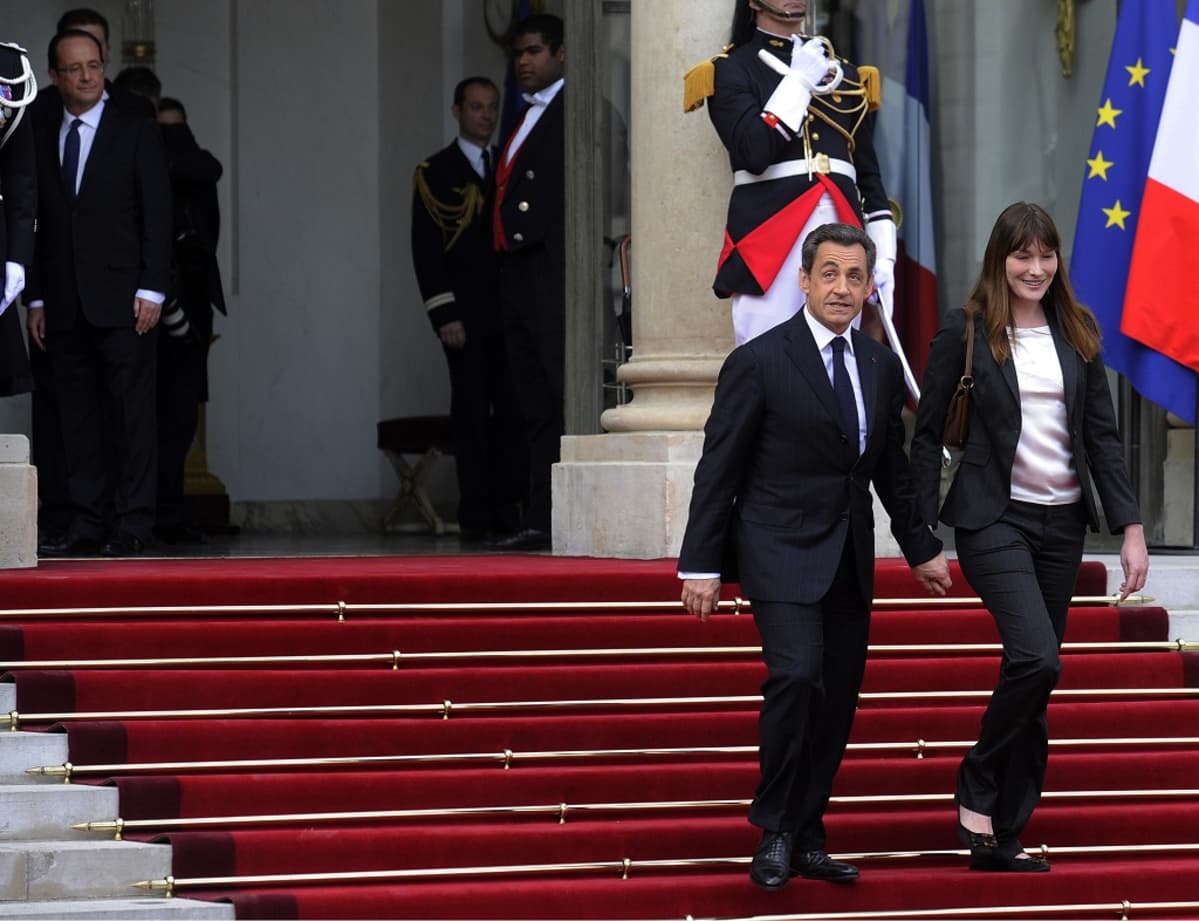 Nicolas Sarkozy ja Carla Bruni Sarkozy astelevat alas Élysée-palatsin portaita. Tuore presidentti Hollande katsoo heidän peräänsä.