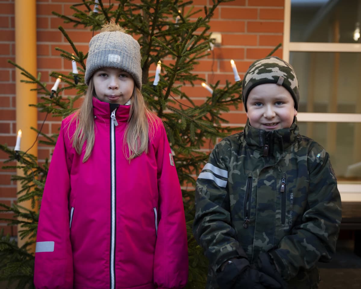 Kaksi lasta poseeraa joulukuusen edessä.