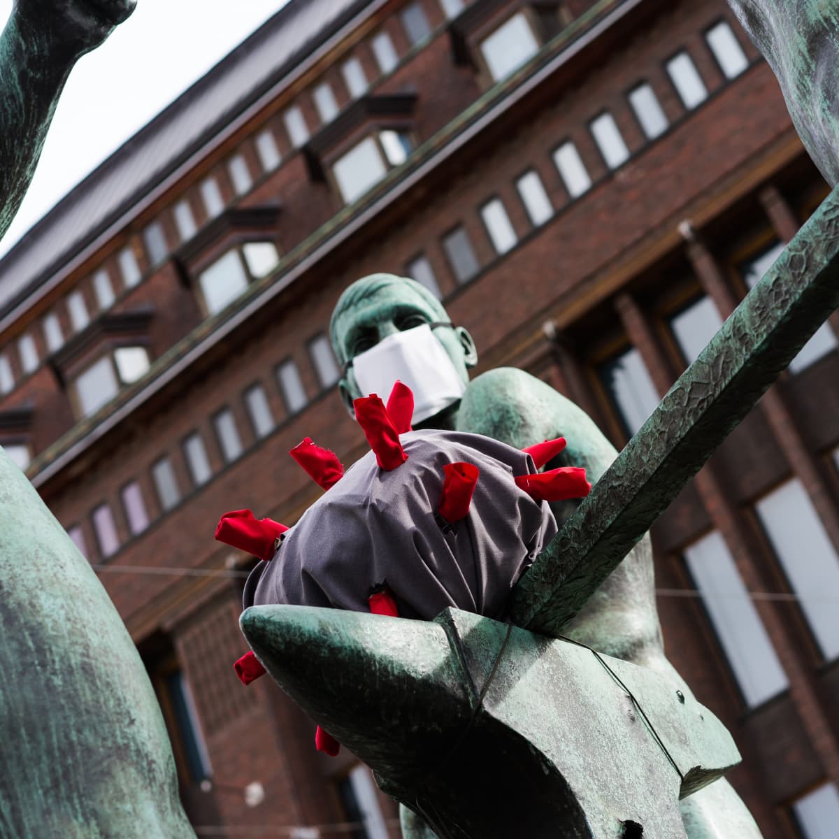 Kolmen sepän patsaan hahmoit takovat koronavirusta 31.3.2020.