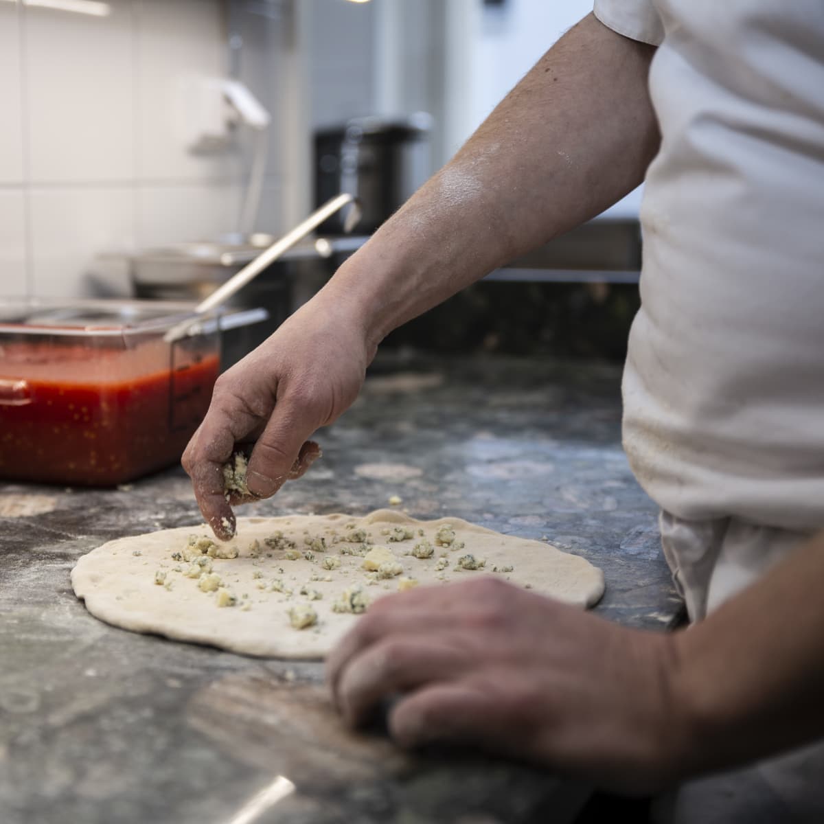 Kokki laittaa sinihomejuustoa pizzan päälle.
