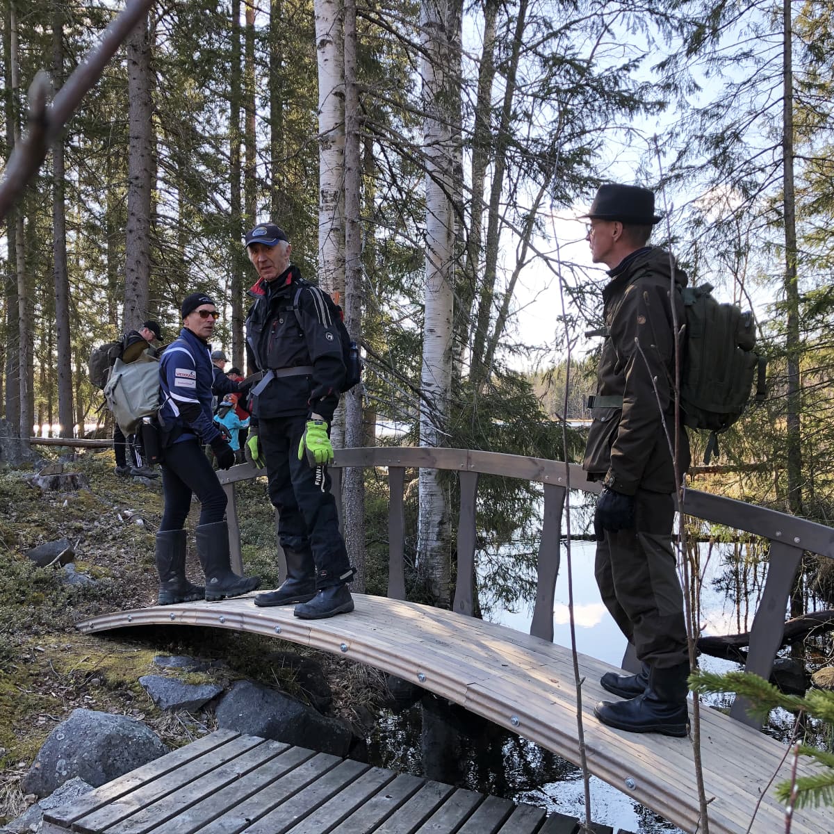 Kuvassa miehiä metsäreitillä sillalla seisomassa