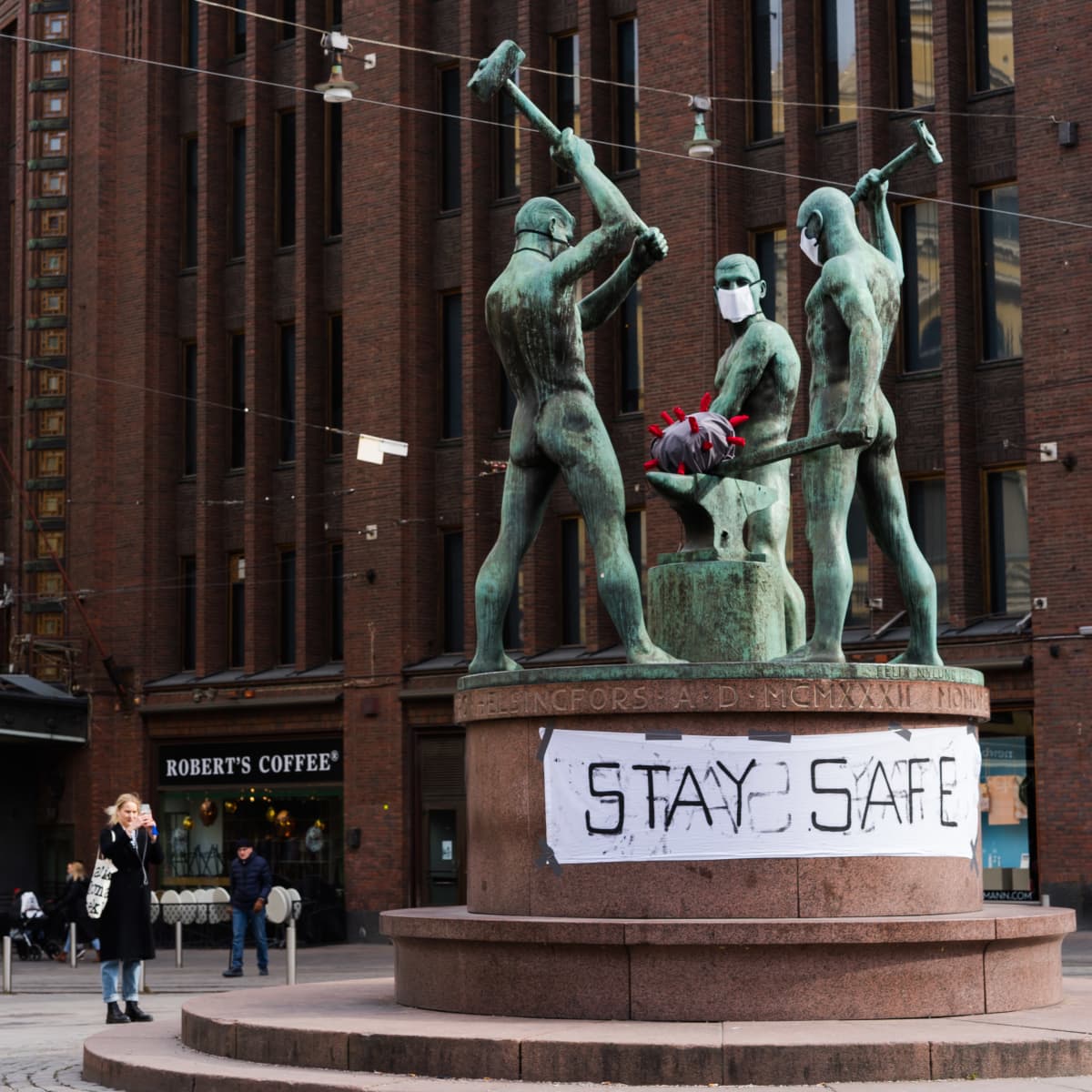 Nainen kuvaa kolmen sepän patsasta, jolla on kasvomaskit.