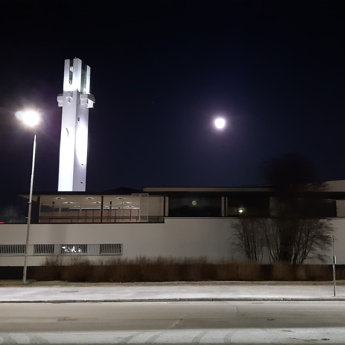 Seinäjoen Lakeuden ristin kirkko ja torni iltapimeällä, taustalla loistaa kuu.