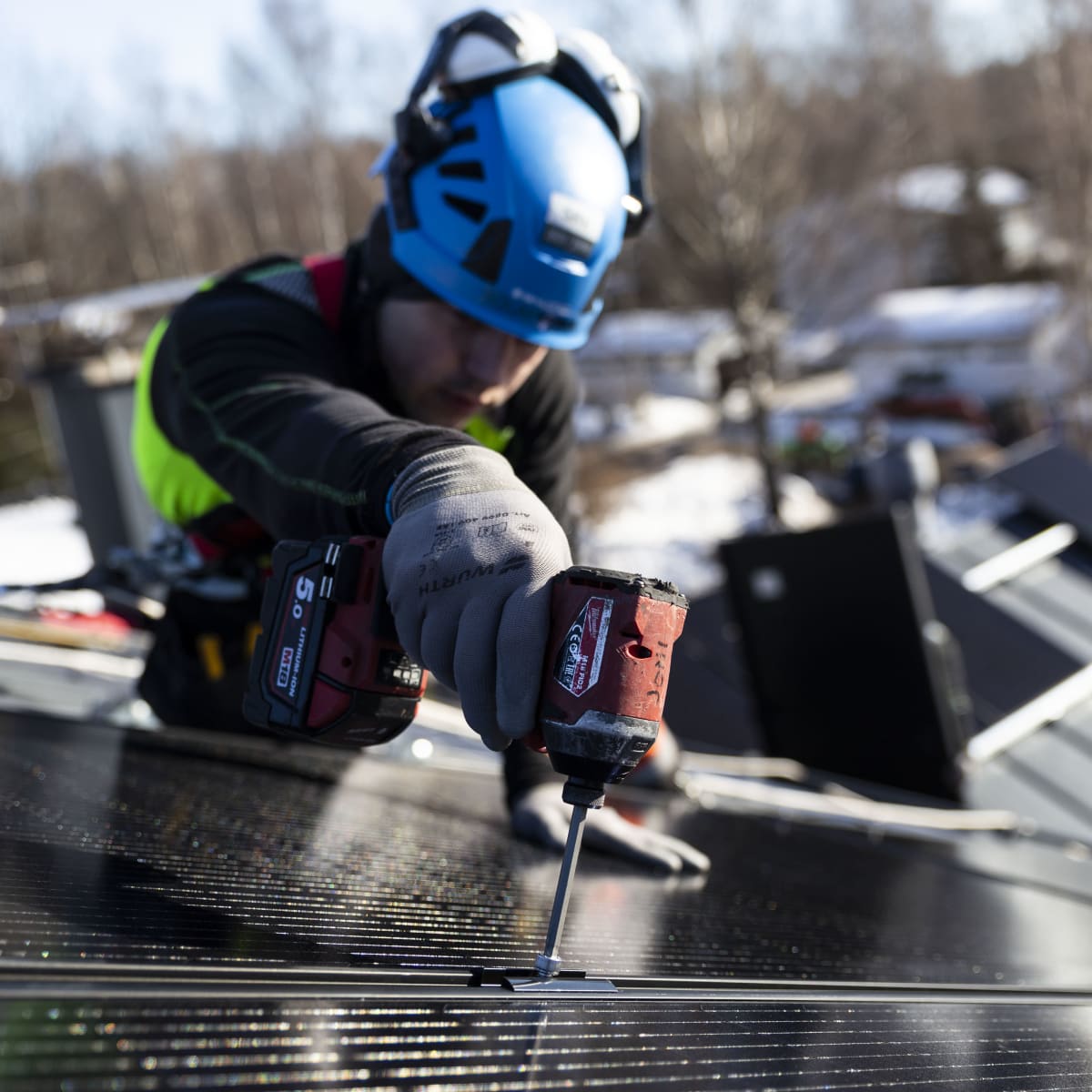 Solarvoima Oy:n asentaja Joni Särkinen asentaa aurinkopaneeleja omakotitalon katolle.