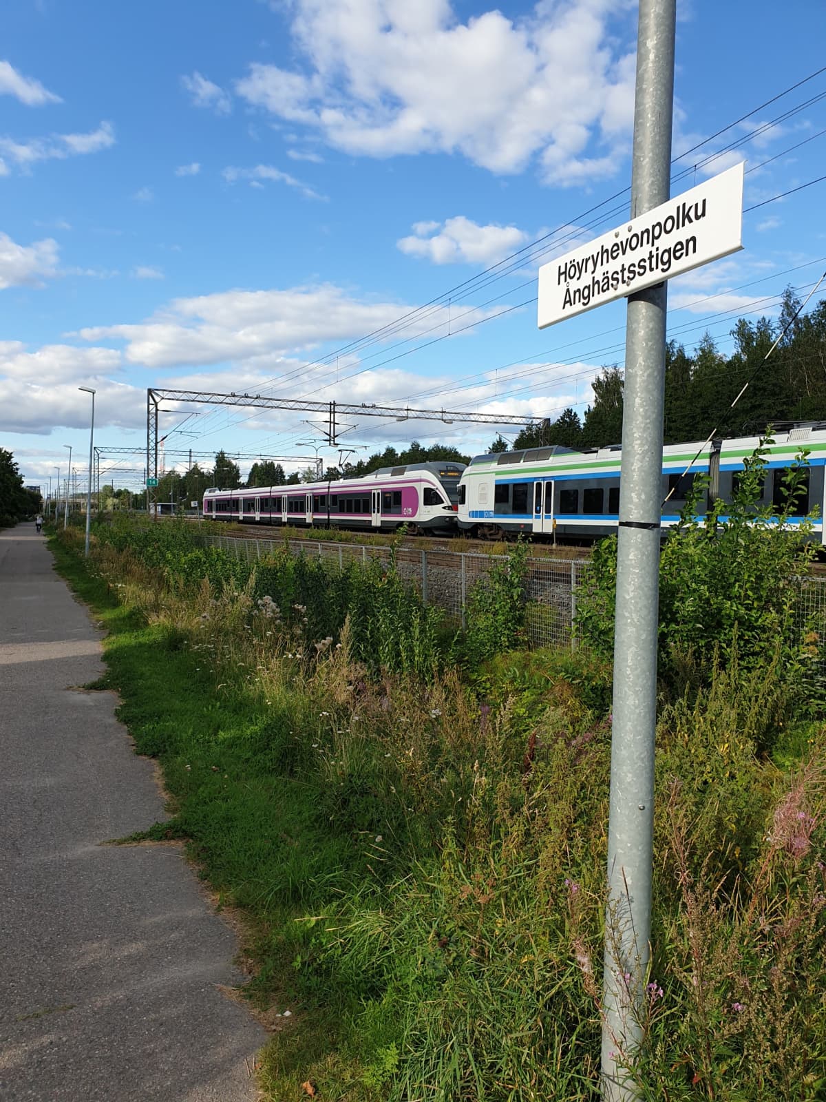 Katukyltti, jossa lukee Höyryhevonpolku. Taustalla junia.
