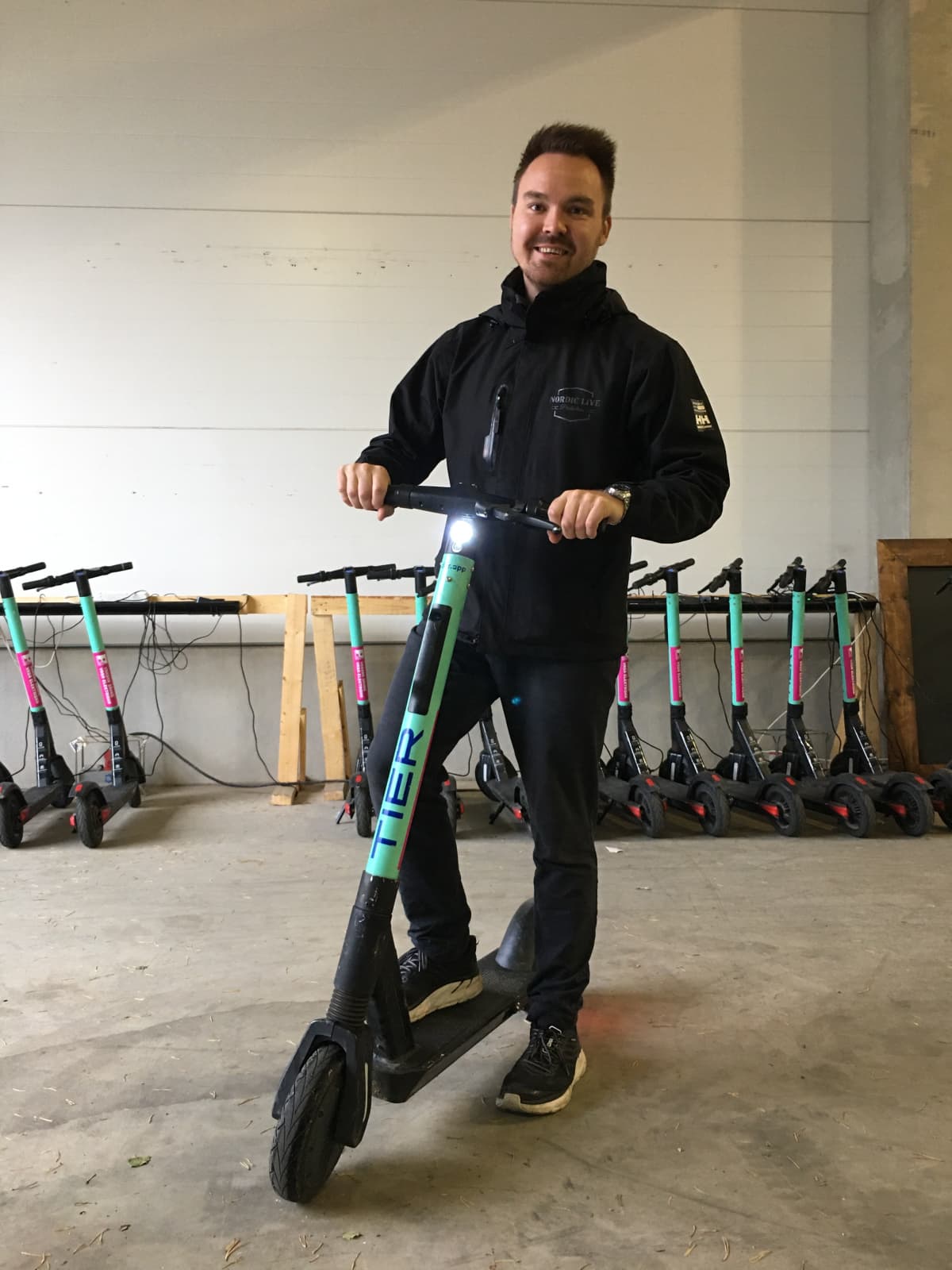Tommi Mäki nojaa sähköpotkulautaan varastotiloissa Vaasassa