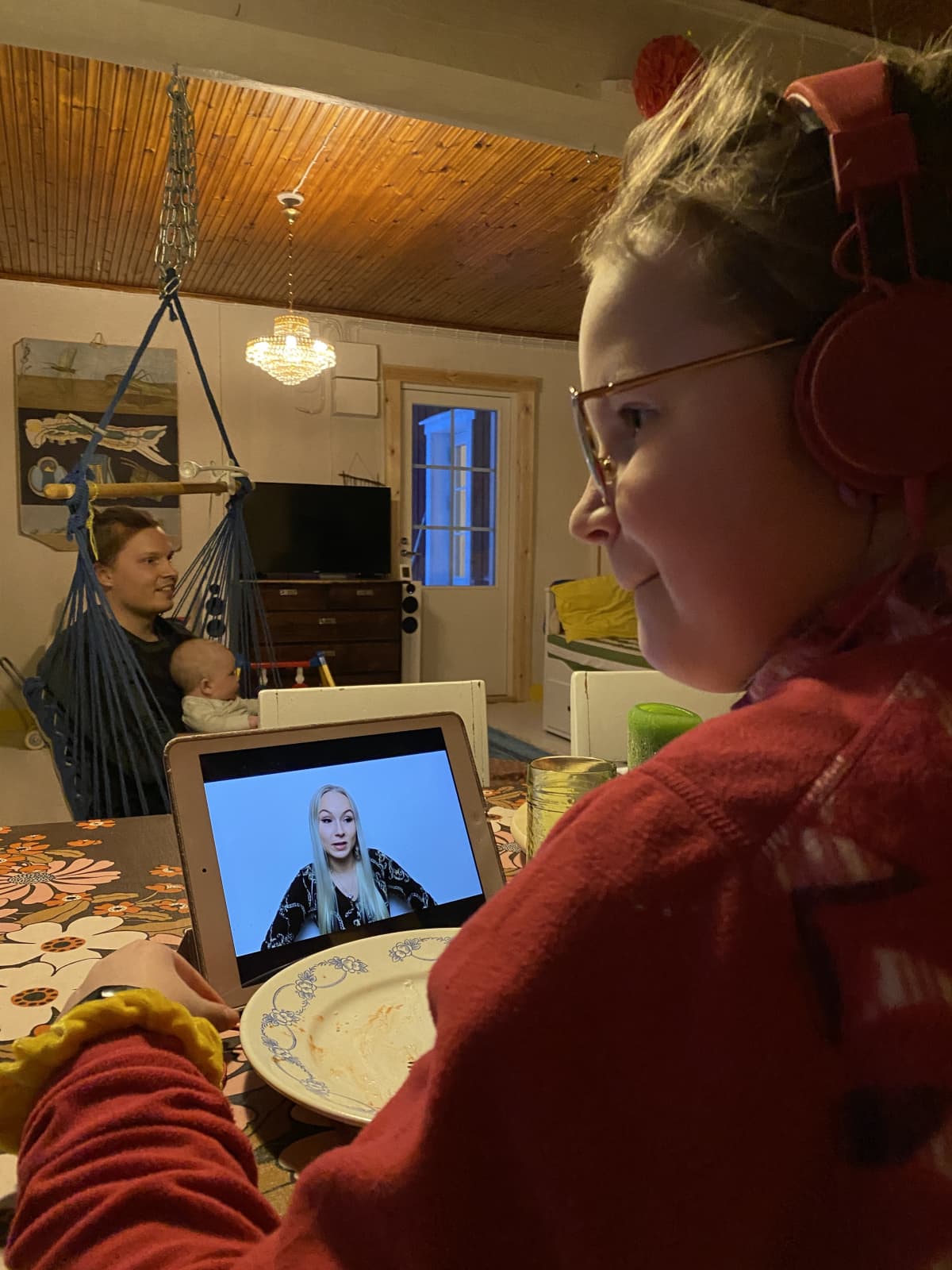 Milli katsoo tabletilta tubettajaa. Takana näkyvät isä-Antti ja Aatos-vauva.