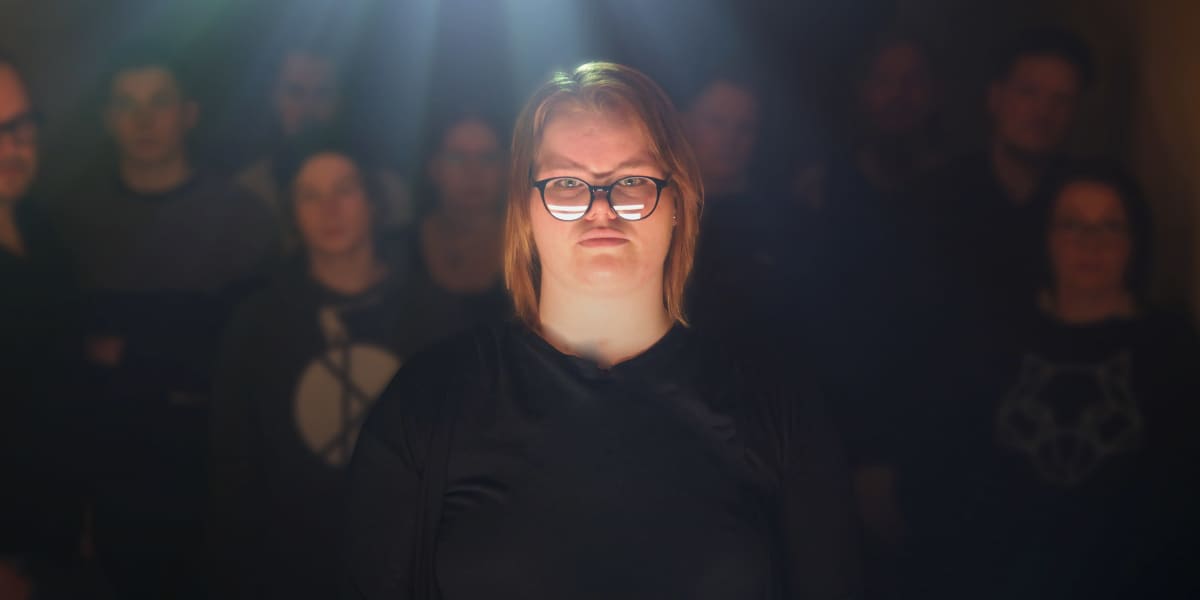Nainen katsoo kohti kameraa ja taustalla on muita ihmisiä.