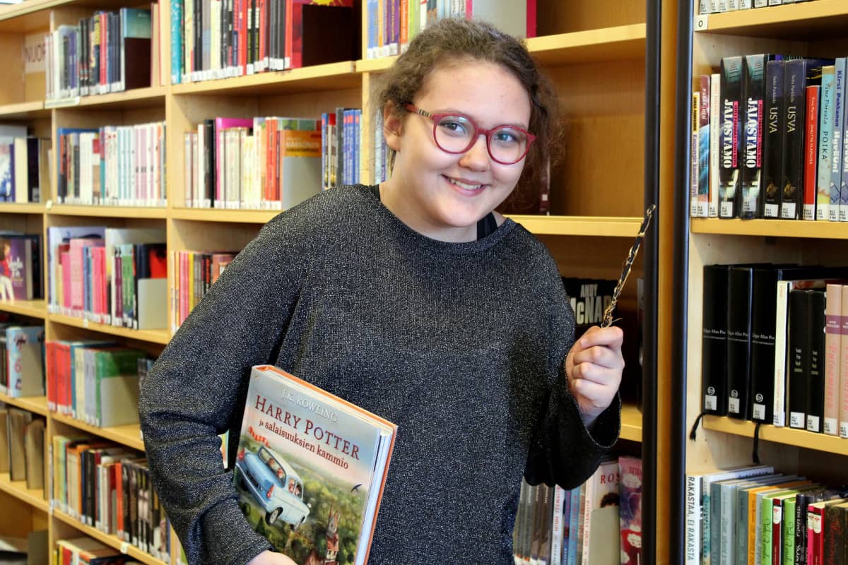 Aida Kankaanpää kirjastossa taikasauva kädessään ja Harry Potter -kirja kainalossaan.
