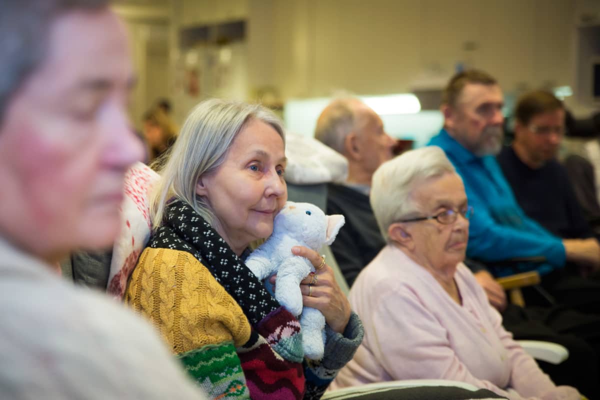 69-vuotias Maria Sandvik nauttii musiikista pehmolelukissan kanssa.