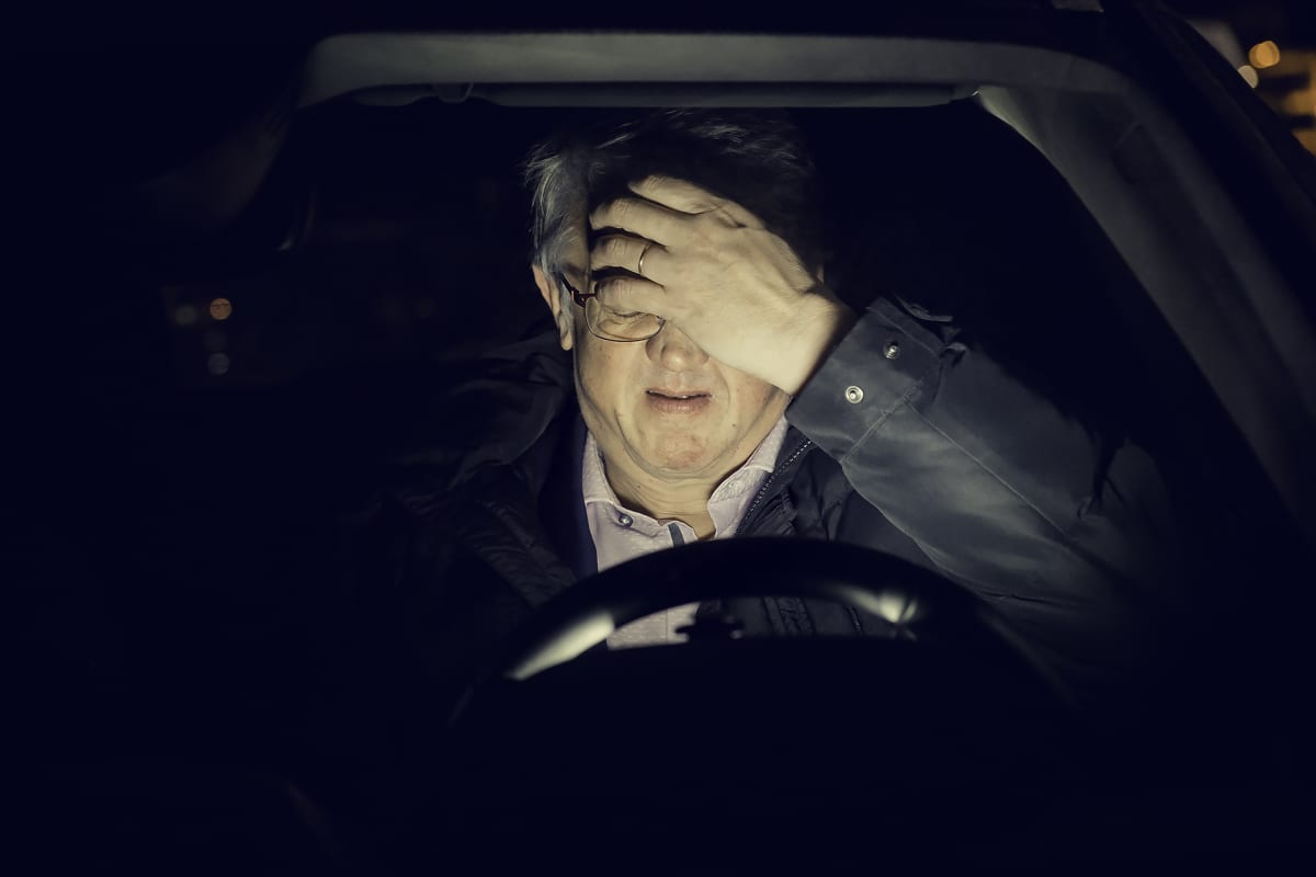 Juha Rehula istuu autossa pimeyden keskellä käsi otsalla.