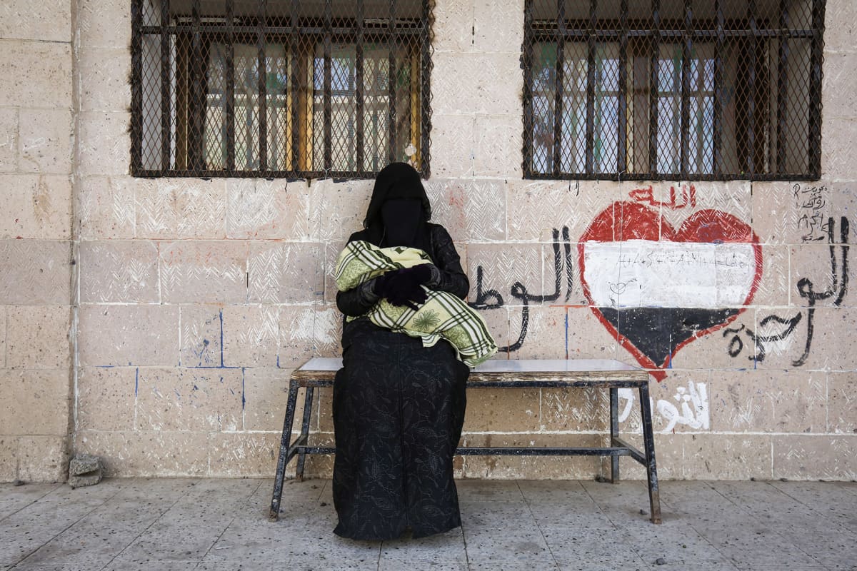 Jemeniläinen burkaan pukeutunut nainen vauva sylissään odottaa ruoka-apua.