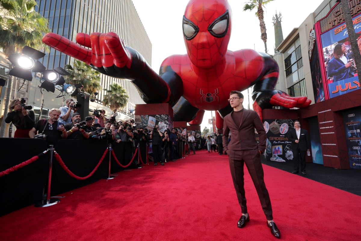 Tom Holland punaisella matolla suuren Hämähäkkimies-veistoksen edessä.