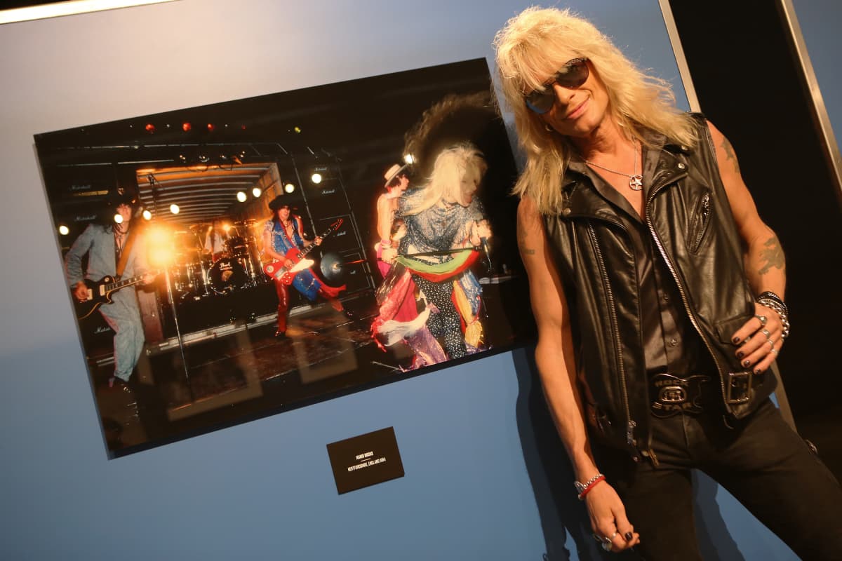Michael Monroe poseeraa Justin Thomas ottaman valokuvan edessä. Valokuva otettu Up Around the Bend -musiikkivideon kuvauksissa 1984.