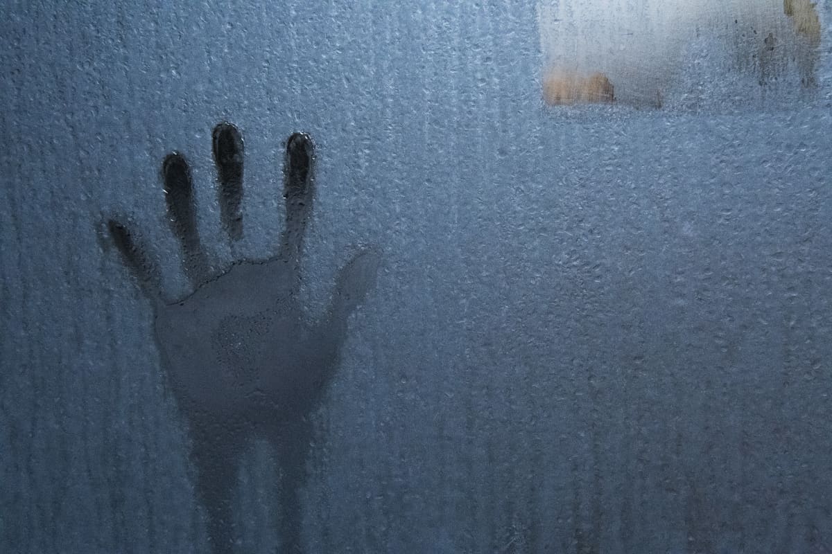 Käden kosketuksen jälki huurteisessa lasiseinässä.