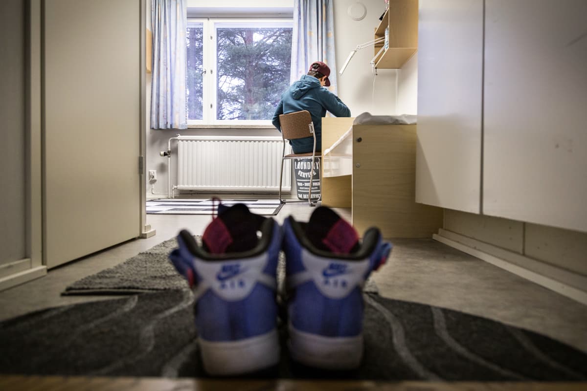 nuori tekee läksyjä pöydän ääressä, etualalla lenkkarit.