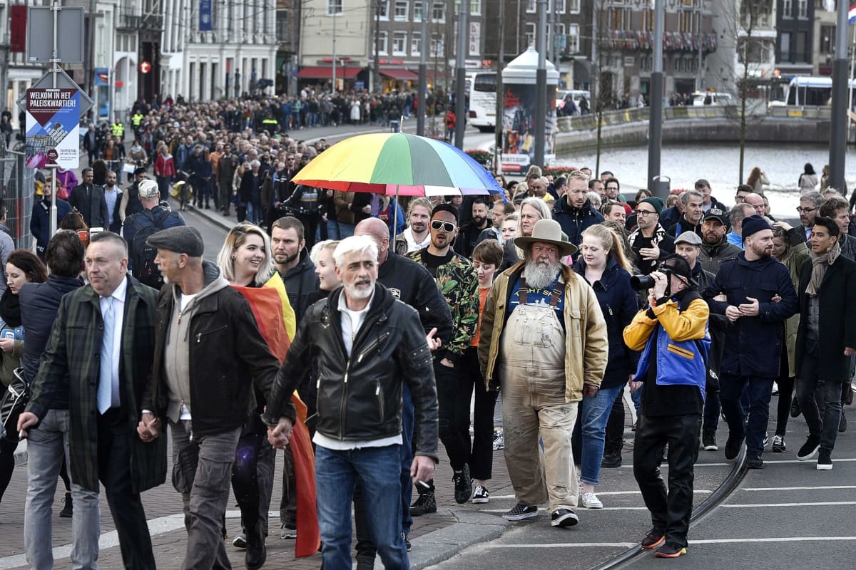 Pitkä jono miehiä kävelee kanavan rannall a toisiaan käsistä pidellen.