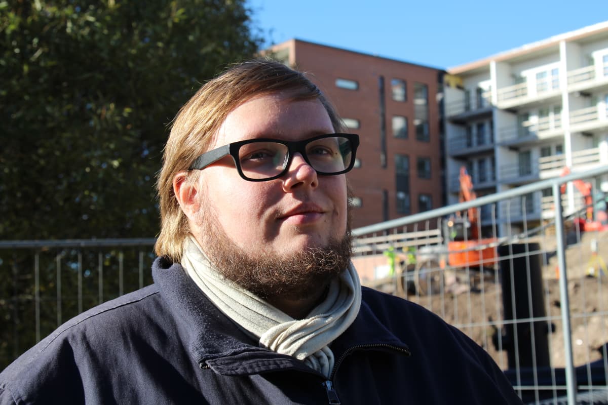 Mies rakennustyömaan aidan vieressä, katsoo kuvasta ulos