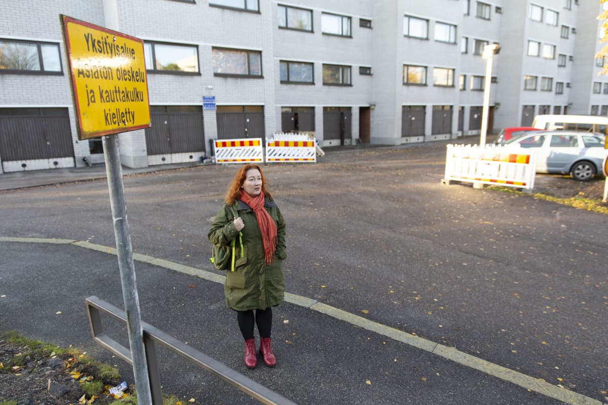 Nina Kuujärvi seisoo pihalla. Taustalla taloyhtiö, jonka kellariin lukkojen taakse hänen postipakettinsa toimitettiin. Kyltti: Yksityisalue - asiaton oleskelu ja kauttakulku kielletty.