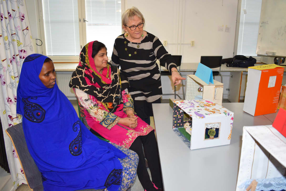 Opettaja Riitta Malila katselee nukkekoteja opiskelijoiden kanssa.