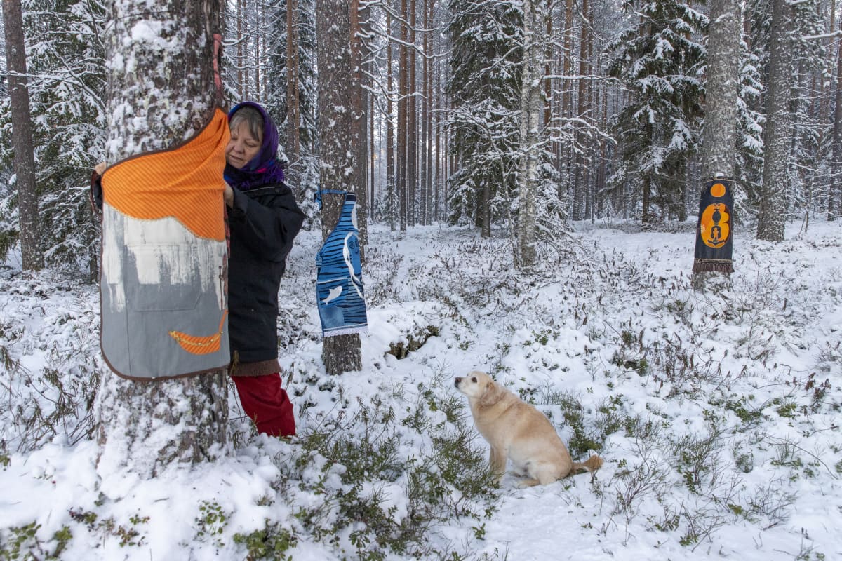 Irma Heiskanen sitoo itse tekemäänsä esiliinaa puun runkoon