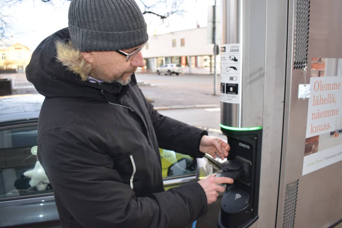 Mies laittaa ladattavan hybridin pistoketta latausasemaan.