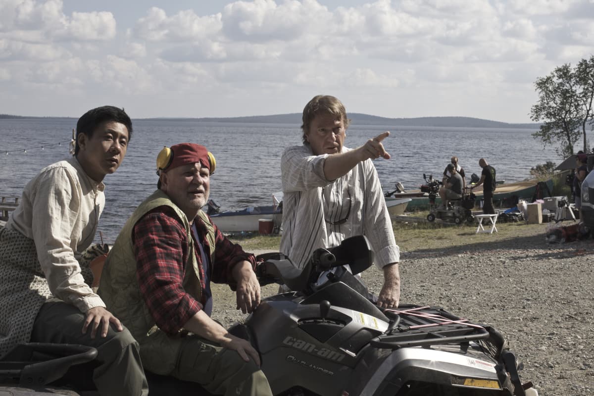 Mika Kaurismäki ohjaa moottoripyörän päällä istuvia Kari Väänästä ja Chu Pak Hongia järven edessä Lapissa.