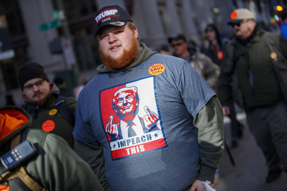 Mies, jonka paidassa on keskisormia näyttävän Donald Trumpin kuva.