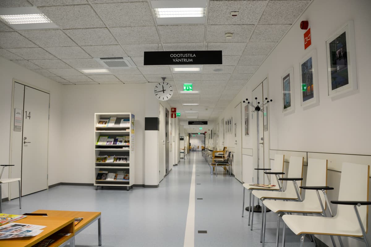 En tom korridor i en hälsocentral. I taker finns en skylt där det står väntrum.