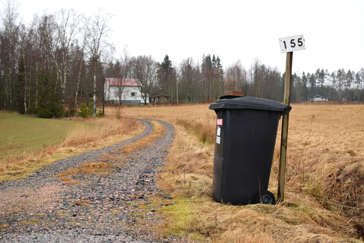 En soptunna vid en uppfart till ett vitt 40-tals hus.