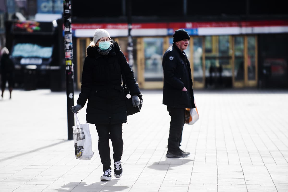 Kuvassa on hengityssuojainta käyttävä nainen, joka kävelee kohti kameraa.