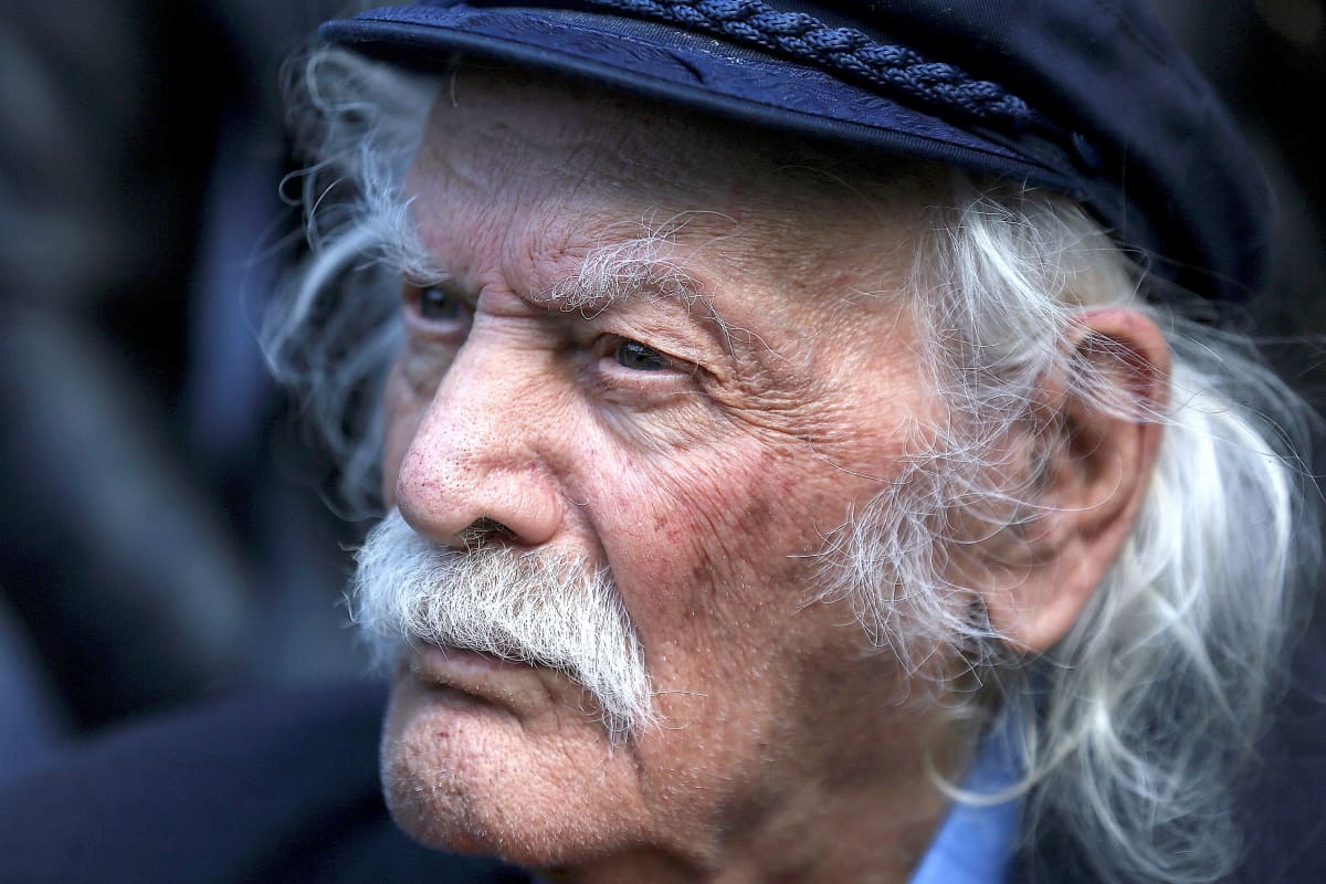 Valkohiuksinen viiksekäs Manolis Glezos katsoo kuvassa tuimasti kuvaajasta vasemmalle.
