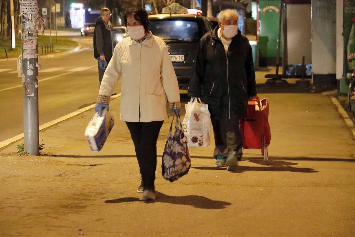 Ihmisiä ostoskassien kanssa hengityssuojaimet kasvoillaan.
