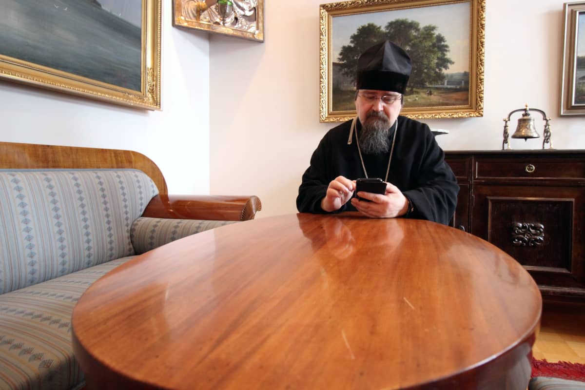 Arkkimandriitta Sergei lukee sähköposteja kännykältä työhuoneessaan.
