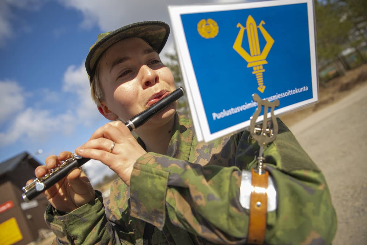 Puolustusvoimien varusmiessoittokuntaan kuuluva Sonja Kohtala soittaa puhallinsoitinta ulkona auringonpaisteessa.