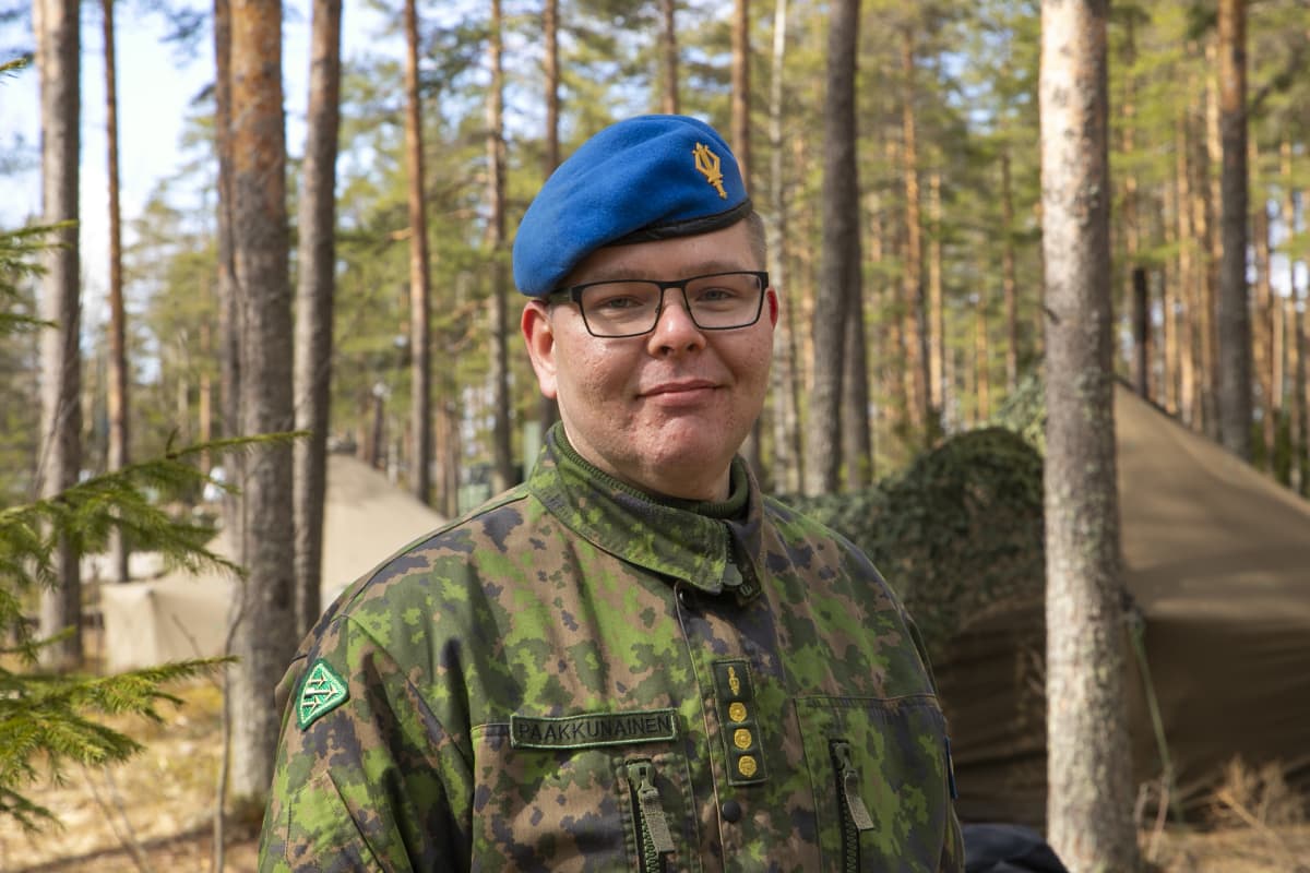 Varusmiessoittokunnan musiikkikapteeni Ville Paakkunainen katsoo kohti kameraa metsässä.